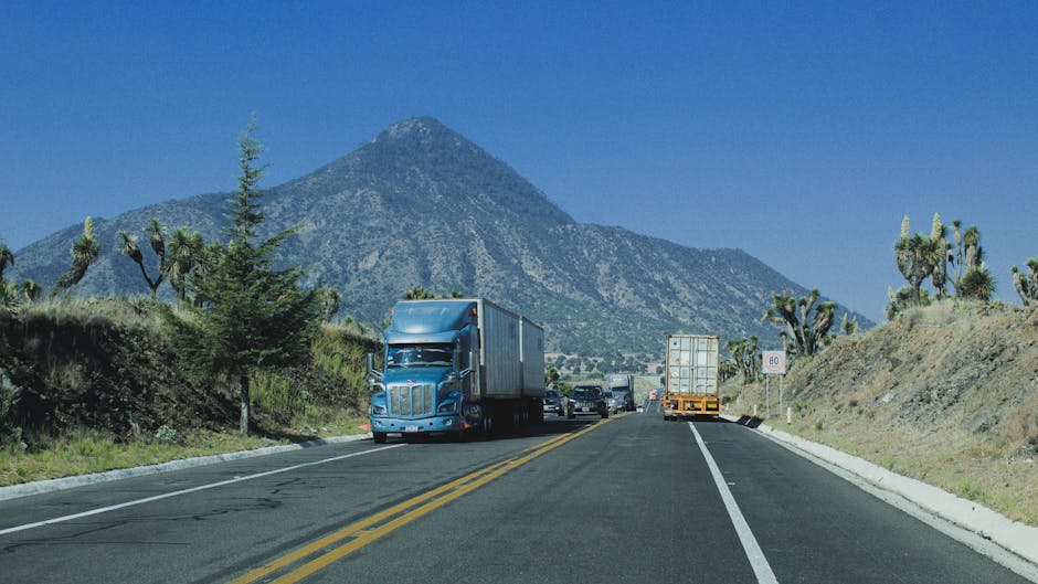Trucks driving on a highway with a mountain backdrop under a clear blue sky.