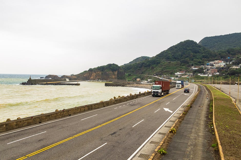 Trucks traveling on a coastal road with beautiful mountain and ocean views, enhancing logistics imagery.